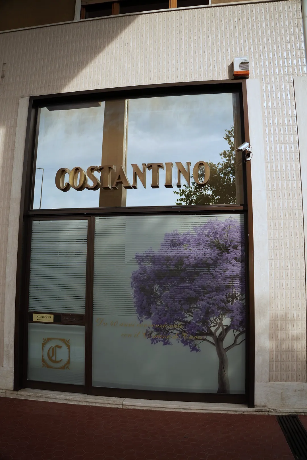La vetrina dell'agenzia con la scritta Costantino in ottone e il glicine in fiore